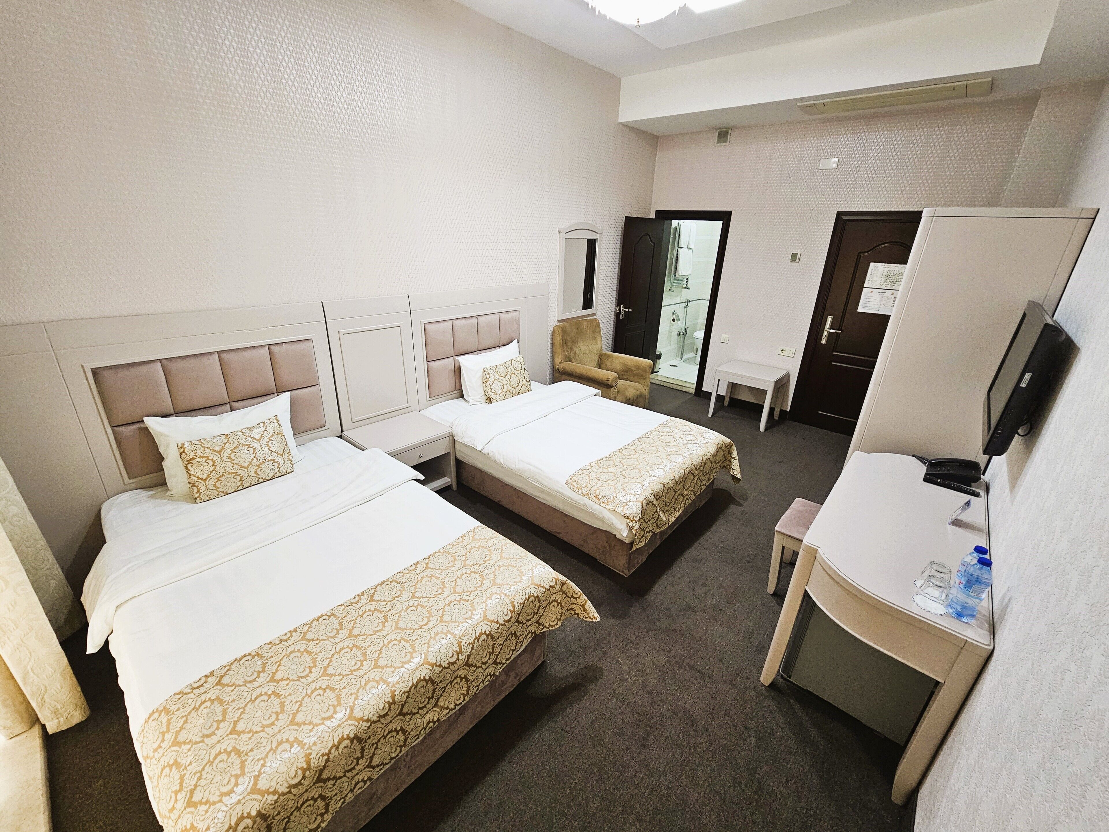 A hotel room with two beds, a desk, a chair, a TV, and a bathroom visible through an open door.