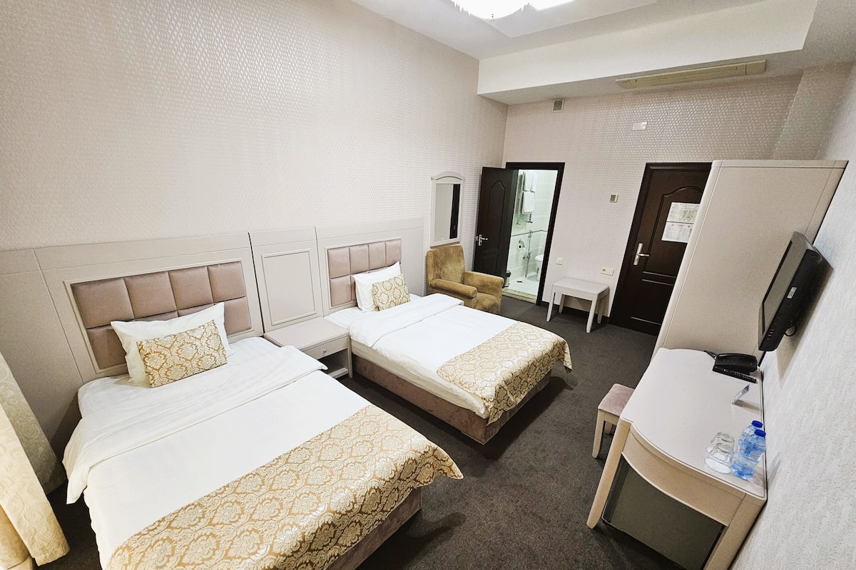 A hotel room with two beds, a desk, a chair, a TV, and a bathroom visible through an open door.