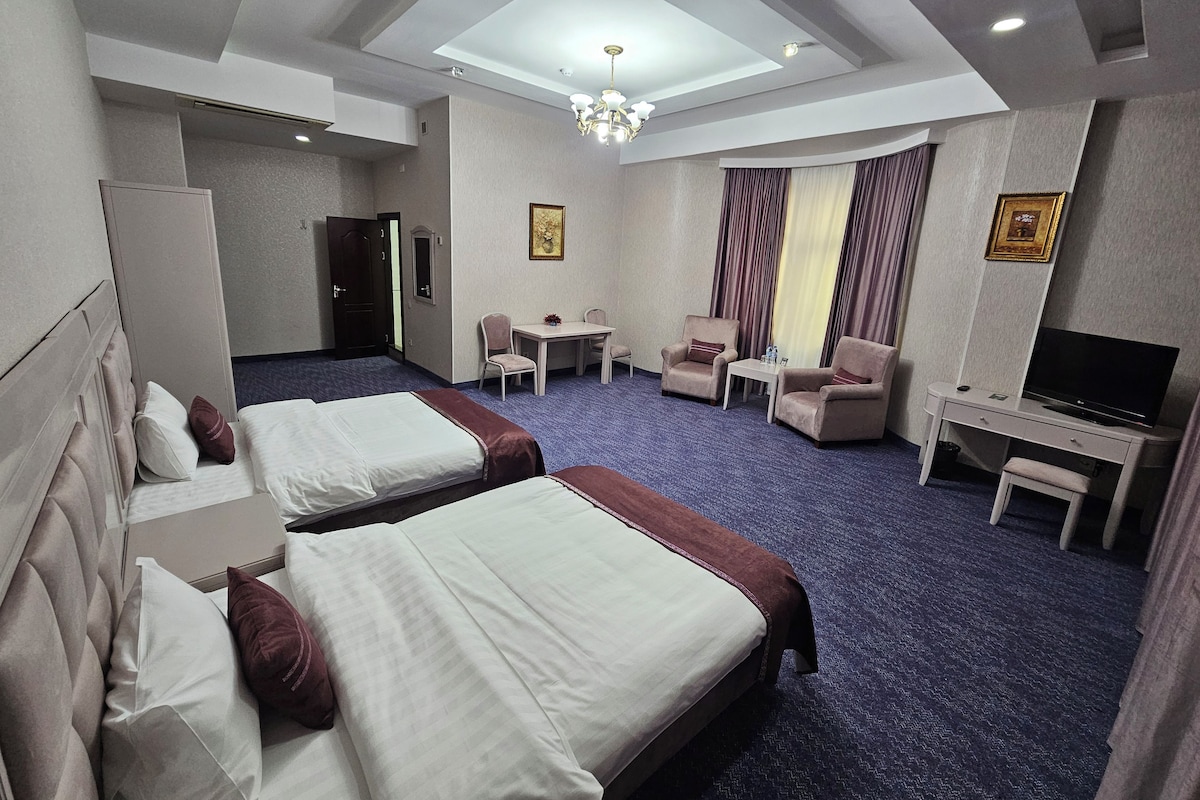 A hotel room with two beds, a desk, a TV, and a seating area.
