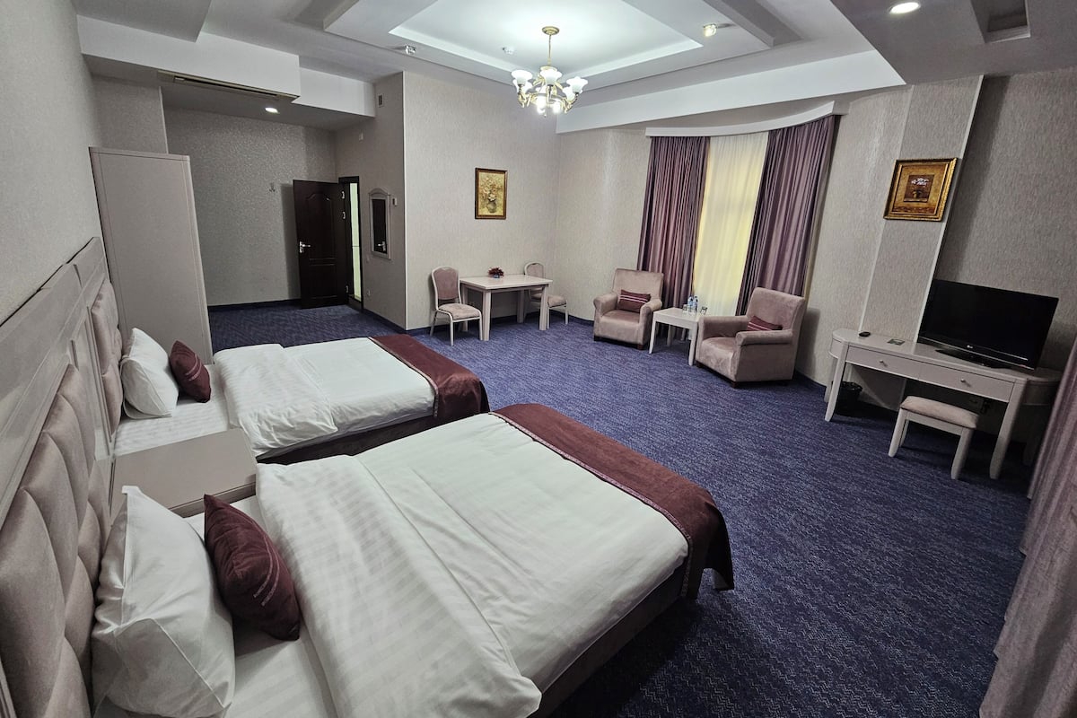A hotel room with two beds, a desk, a TV, and a seating area.