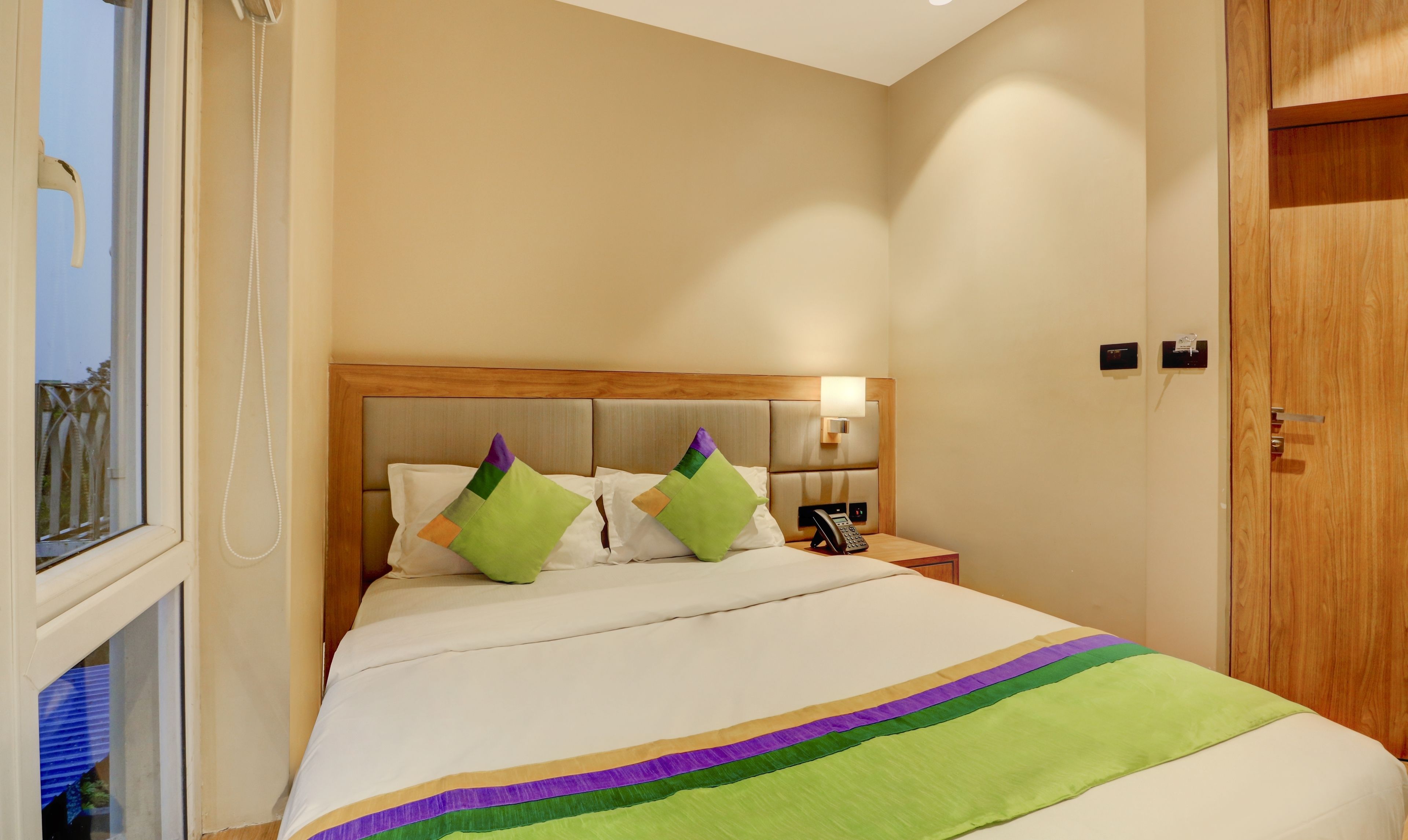 A hotel room with a bed, a bedside table with a phone, and a wooden wardrobe.