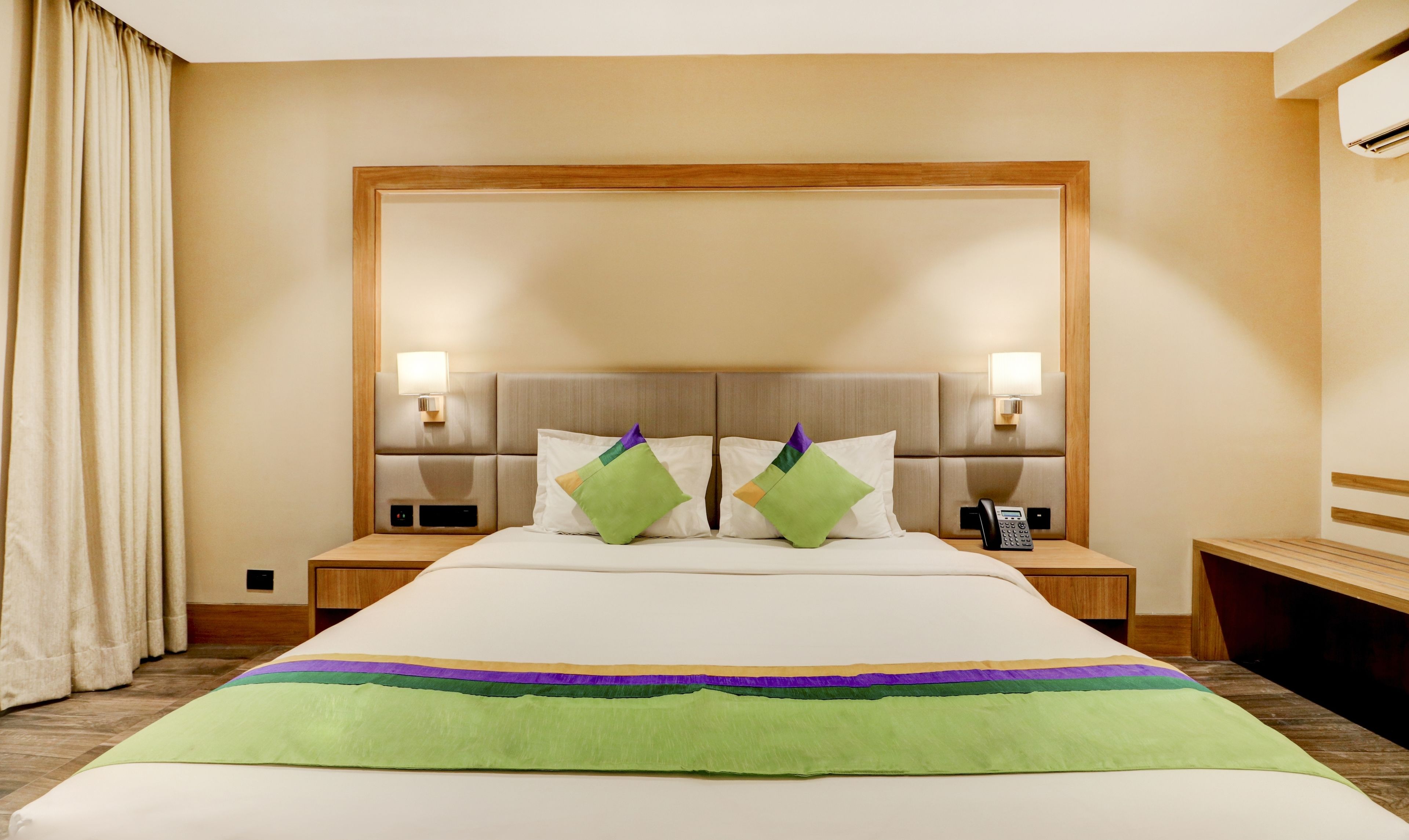 A hotel room with a large bed, two bedside tables, a telephone, and a wall-mounted light fixture.