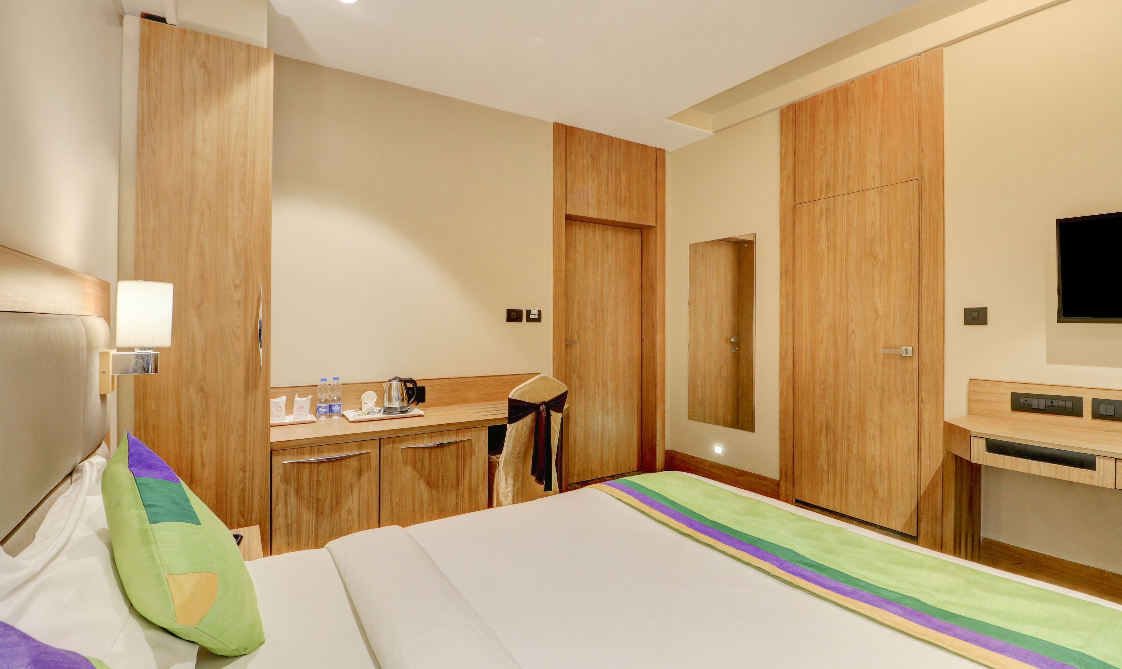 A hotel room with a bed, a desk, a chair, a mirror, and a television.