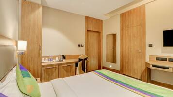 A hotel room with a bed, a desk, a chair, a mirror, and a television.