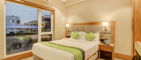 A hotel room with a large bed, a bedside table with a phone, and a window with a view of buildings.