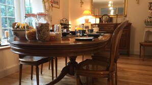Comedor con mesa de madera dispuesta para cuatro personas, rodeada de sillas. Hay frascos de comida sobre la mesa, una lámpara y un espejo encima.