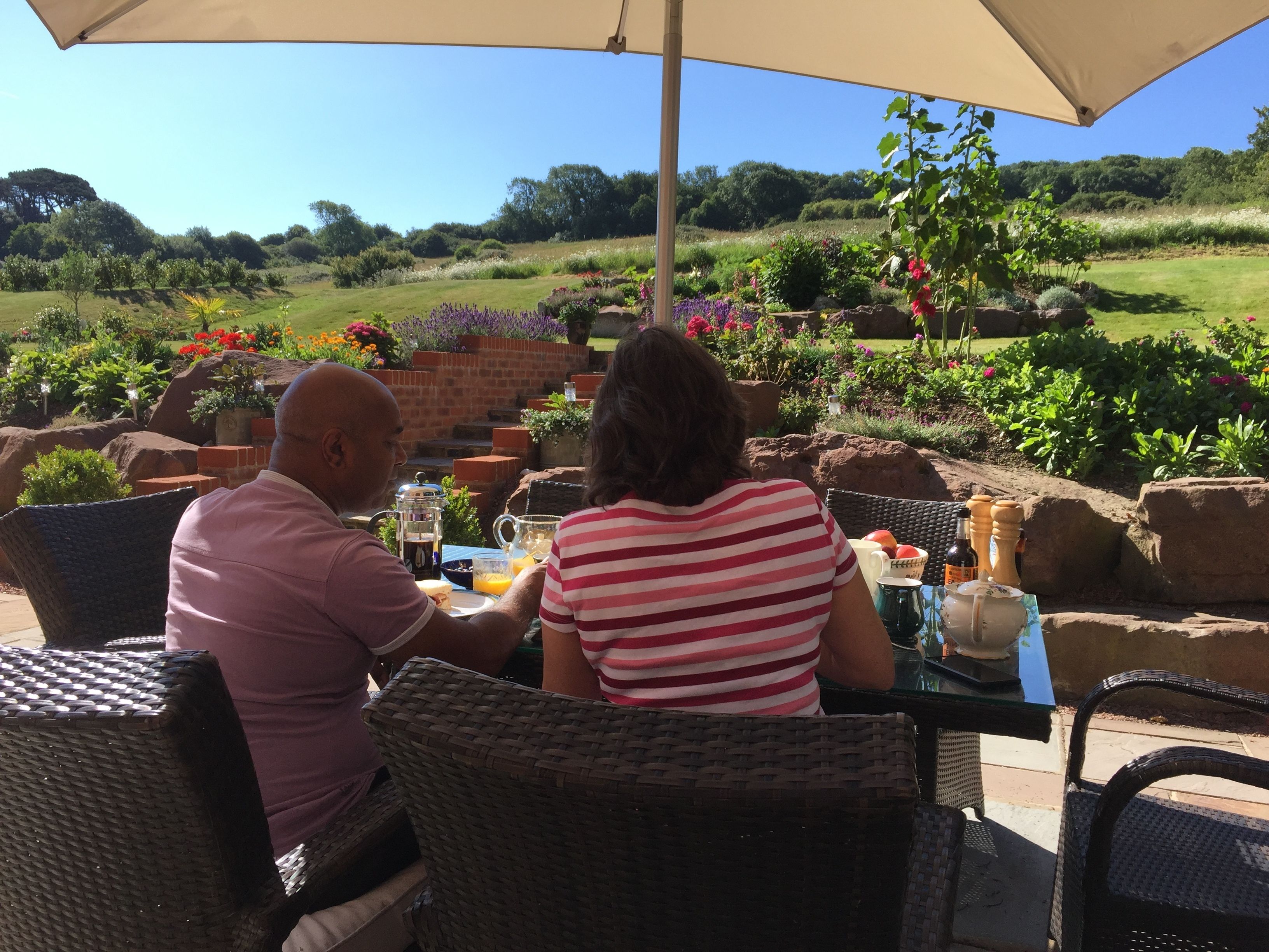 A couple dining at an outdoor table with a view of a landscaped garden and hills.