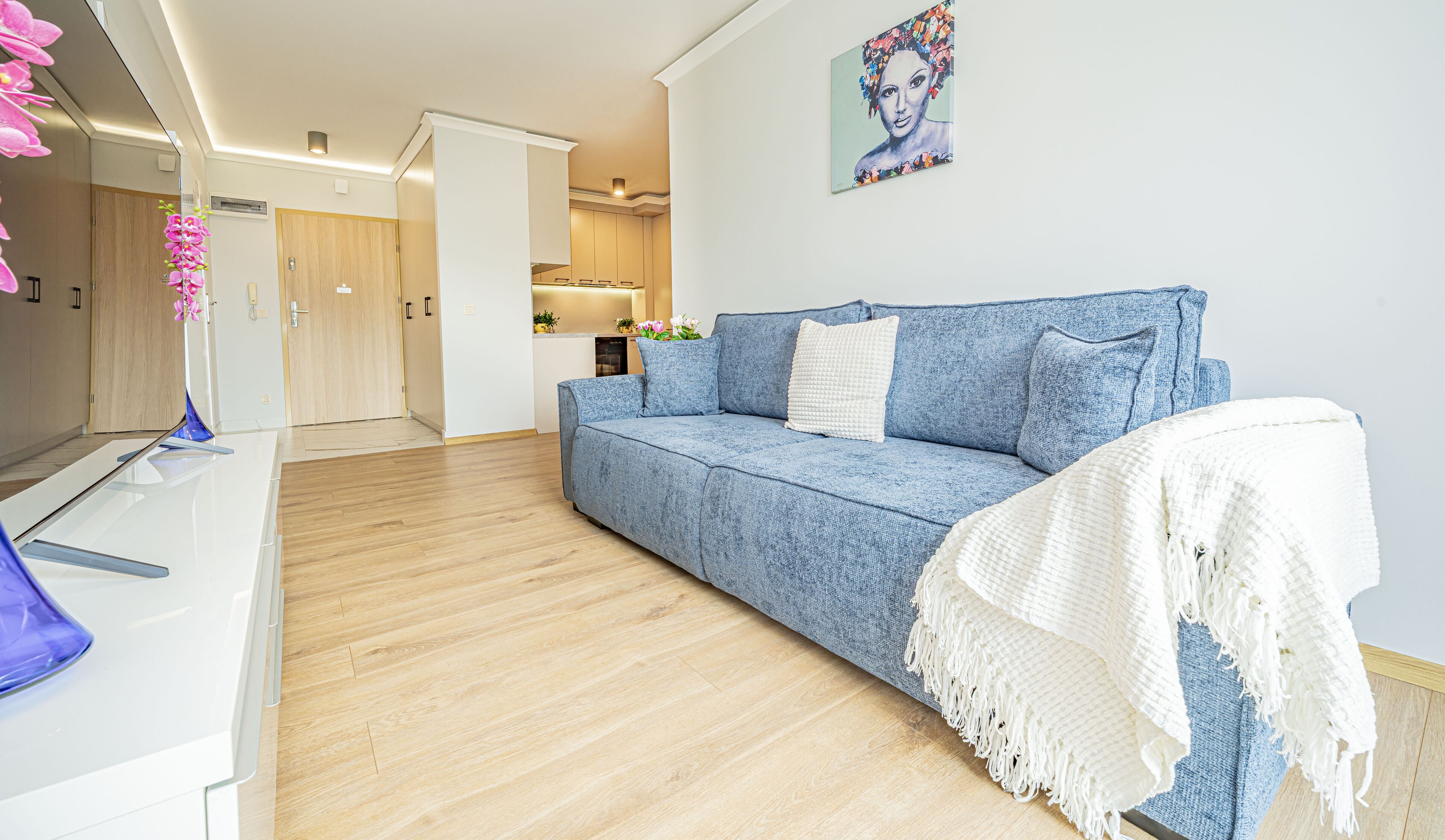 Un salon moderne avec un canapé bleu, un plaid blanc et un tableau accroché au mur.