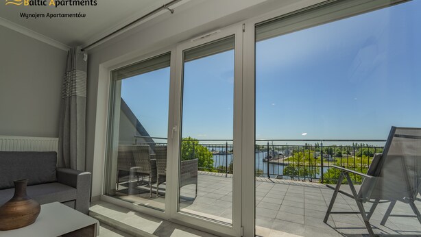 A modern apartment with a large sliding glass door leading to a balcony with a view of a lake and a bridge. - Baltic Apartments - Apartamenty Bałtyk (Swinoujscie)