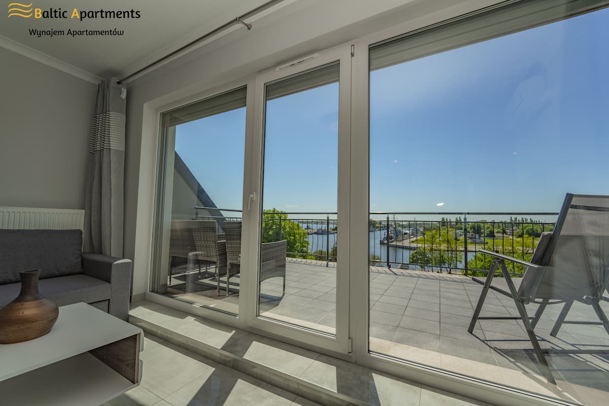 Un apartamento moderno con un amplio ventanal corredera que da a un balcón con vistas a un lago y un puente.