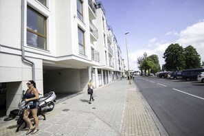A modern building with a covered entrance, a paved sidewalk, and parked vehicles. - Baltic Apartments - Apartamenty Bałtyk (Swinoujscie)