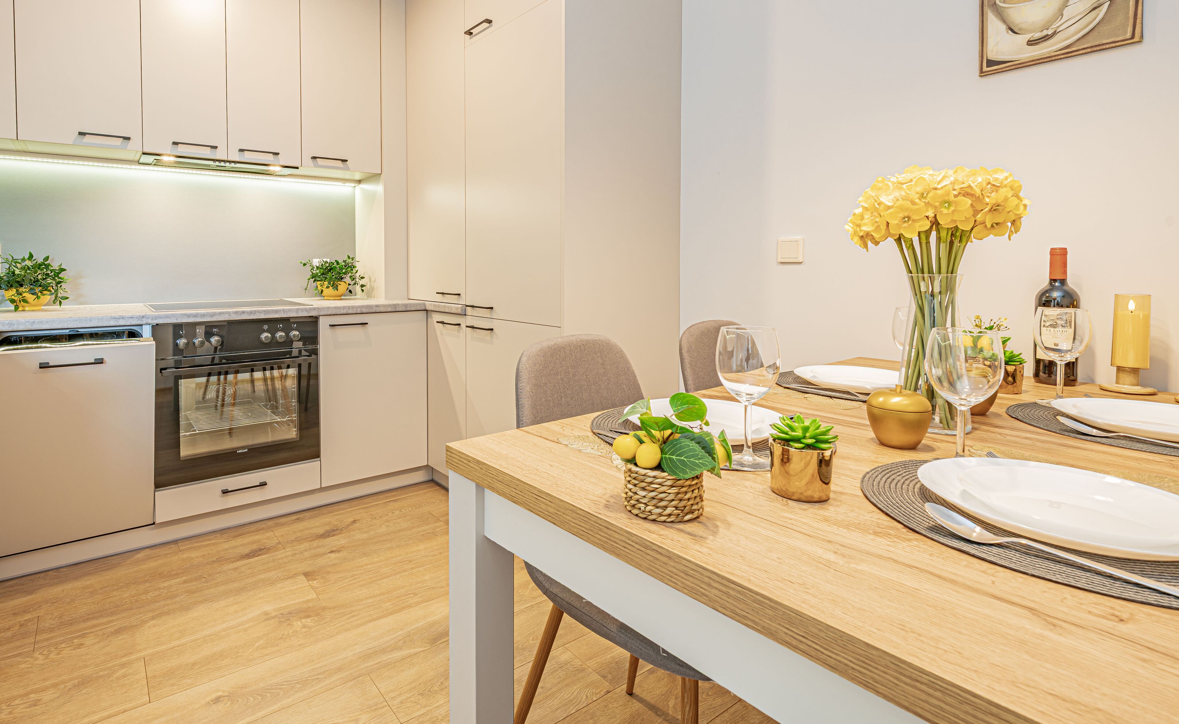 A modern kitchen with a built-in oven and a dining area with a wooden table set for two.