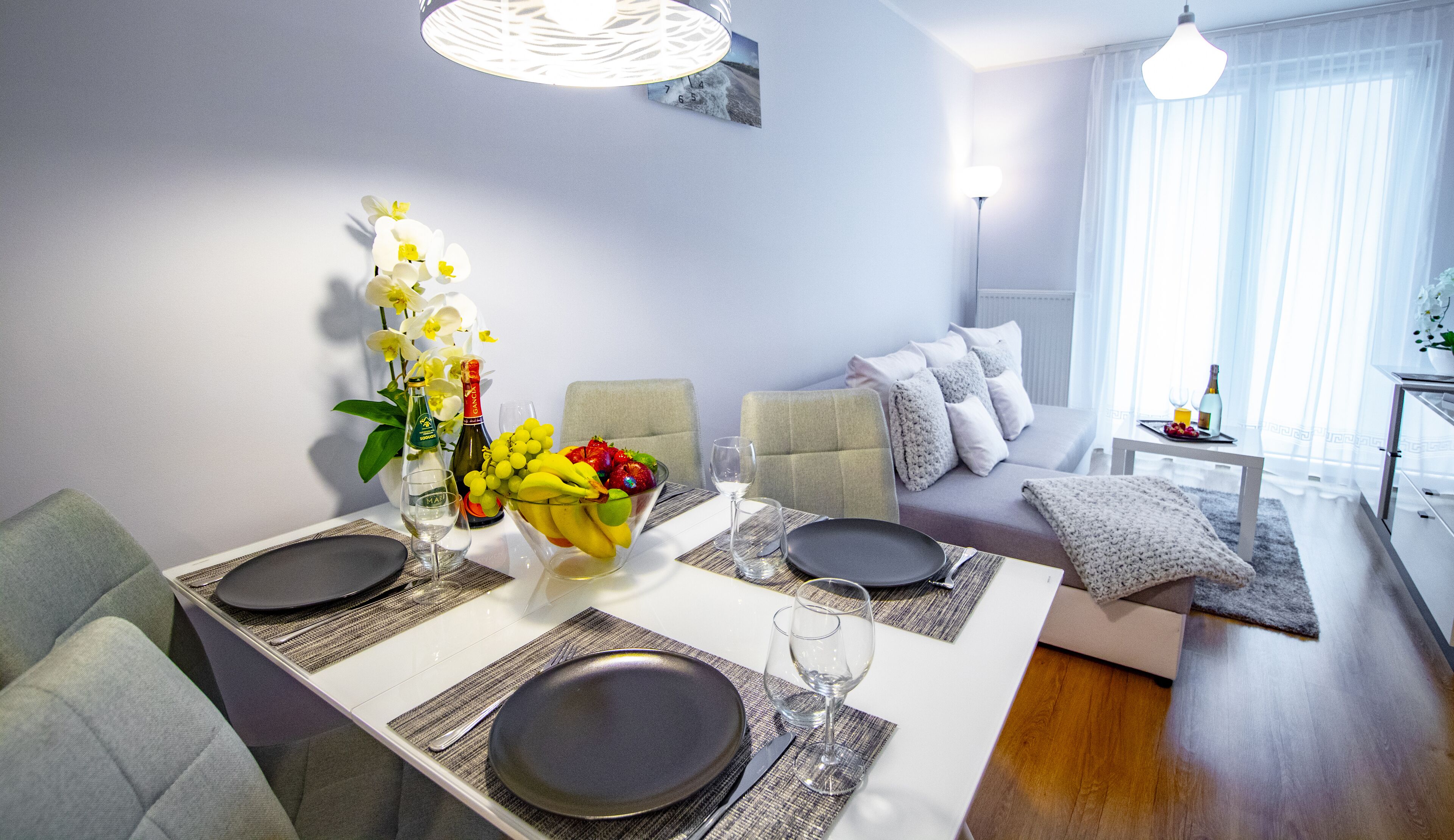 A dining area with a table set for two, a vase of flowers, and a bottle of wine.