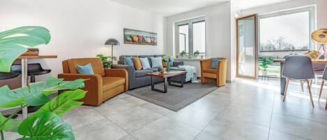 A modern living room with a sofa, armchairs, a coffee table, and a dining area with chairs.