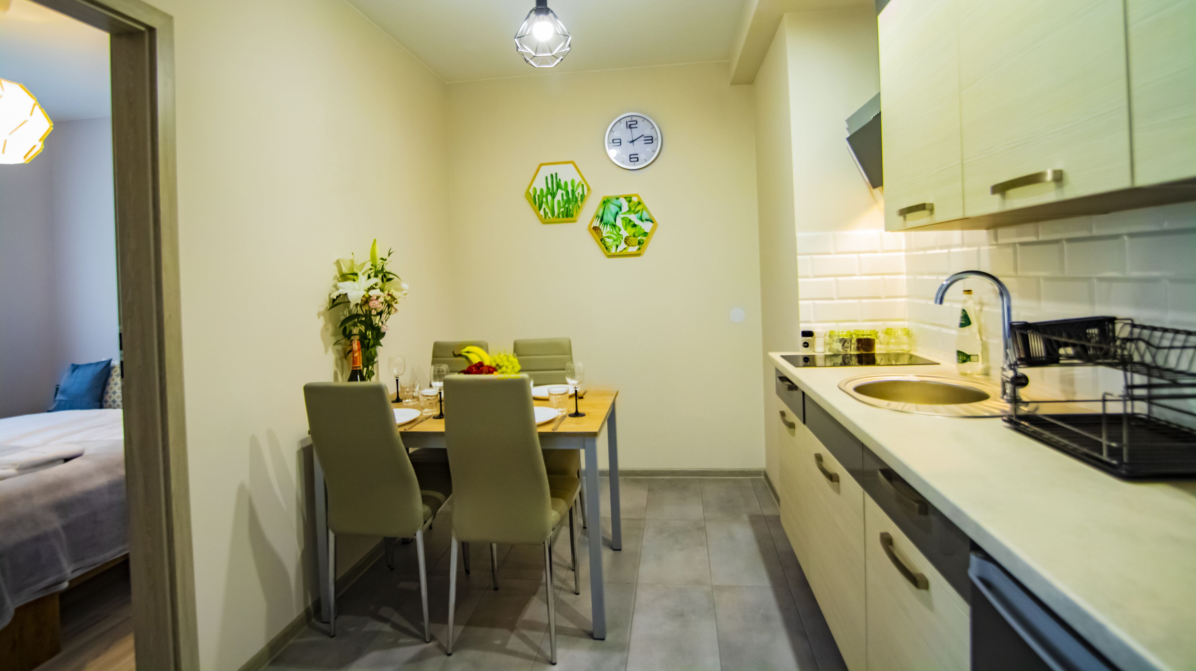 A compact kitchen with a dining area, featuring a sink, cabinets, and a clock on the wall.