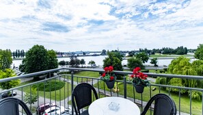 A balcony with a view of a river, greenery, and a bridge in the distance. - Baltic Apartments - Apartamenty Bałtyk (Swinoujscie)