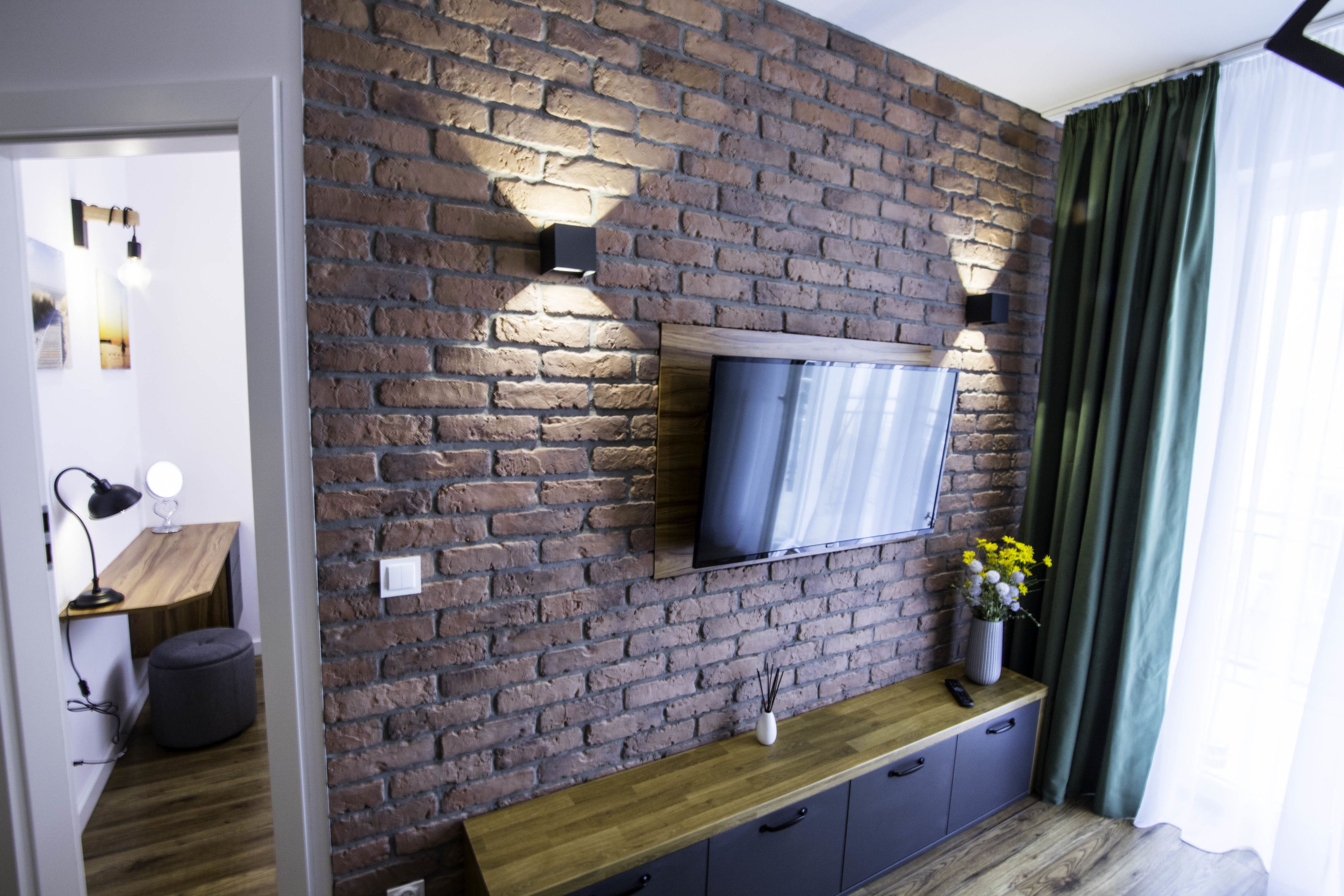 Una sala moderna con pared de ladrillo, televisor de pantalla plana, mesa consola de madera y cortina verde.