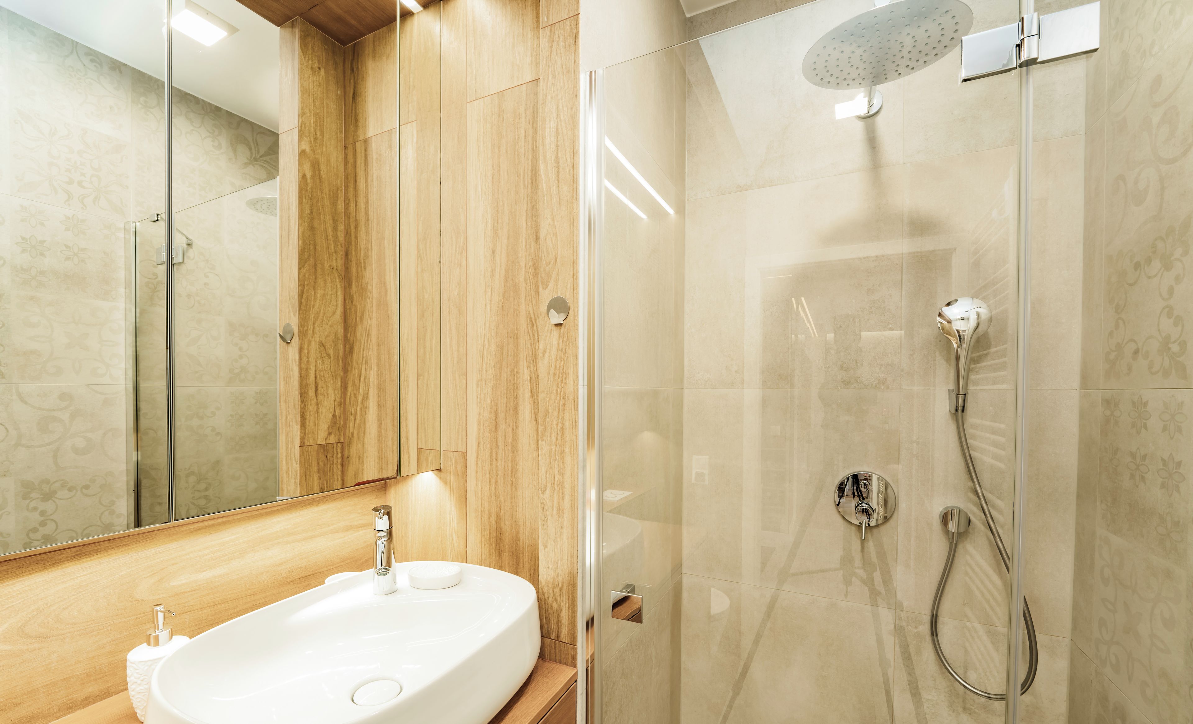 Ein modernes Badezimmer mit einer einteiligen Glasdusche, einem Holzwaschtisch und einem großen Spiegel.
