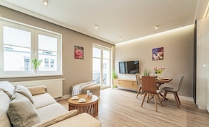 Un salon moderne comprenant un canapé, une table à manger et des chaises, un téléviseur et des œuvres d’art accrochées aux murs.