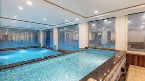 An indoor swimming pool with clear glass walls, tiled flooring, and recessed ceiling lighting. - DLS Hotels on the Ganges (Narendranagar)