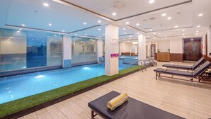 A modern indoor swimming pool area with a glass wall, lounge chairs, and a sign indicating a relaxation area. - DLS Hotels on the Ganges (Narendranagar)