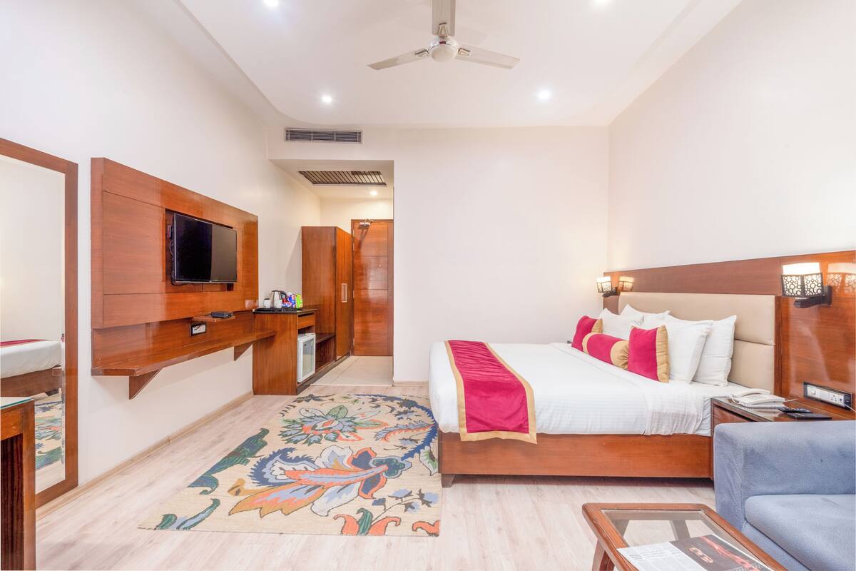 A hotel room with a bed, a TV mounted on the wall, a desk, and a ceiling fan.