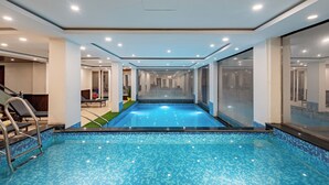 An indoor swimming pool with clear blue water, surrounded by walls with glass panels and a ceiling with recessed lighting. - DLS Hotels on the Ganges (Narendranagar)
