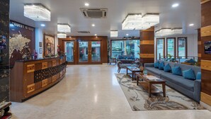 A hotel lobby with a reception desk, seating area, and large windows. - DLS Hotels on the Ganges (Narendranagar)