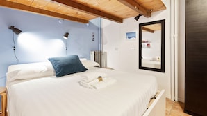 A neatly made bed with white linens and a blue pillow, a bedside table with a lamp, and a mirror on the wall. - Cosy Nest Isola District Heart (Milan)