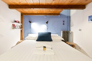 Cozy retreat with a neatly made bed, wooden stool, and bookshelf.