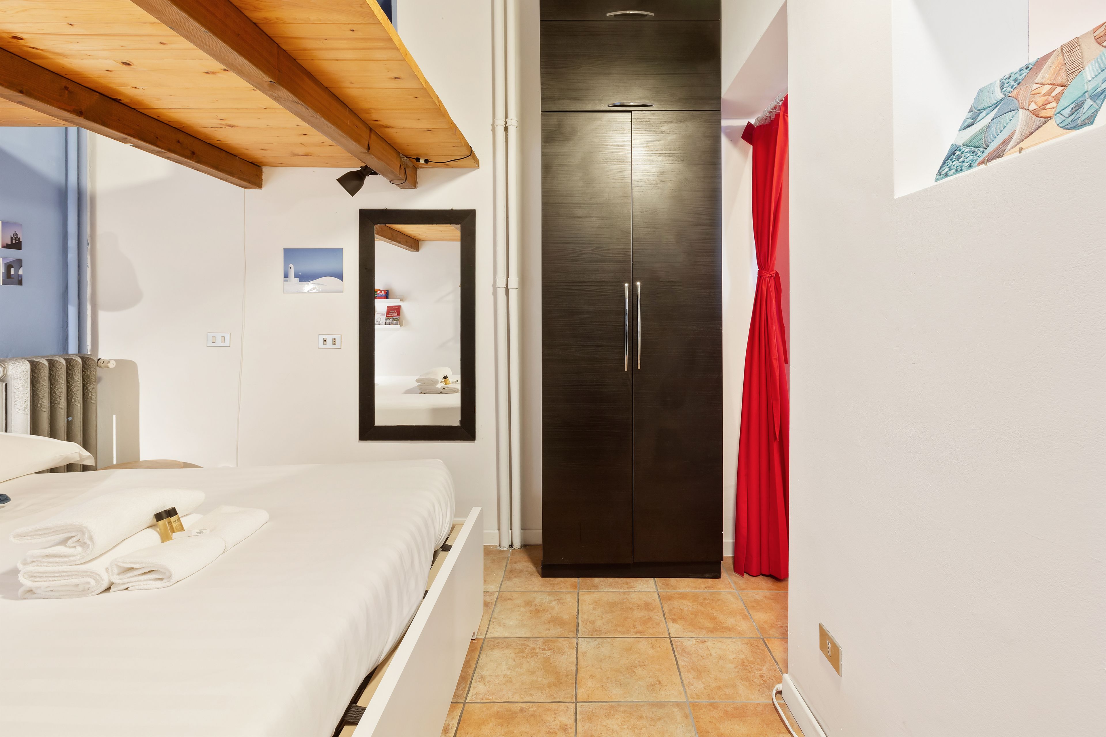 Un dormitorio con cama, armario, espejo y una cortina roja.