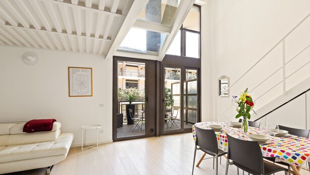 A modern living room with a white sofa, a dining table with a colorful tablecloth, and a staircase leading to an upper level. - Elegant Loft with balcony (Milan)