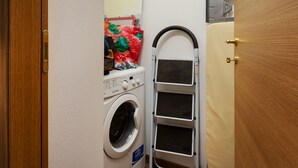 Un área de lavandería compacta con lavadora, tendedero y un estante con ropa doblada.