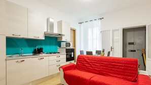 Una cocina compacta con armarios blancos, un microondas y un sofá rojo.