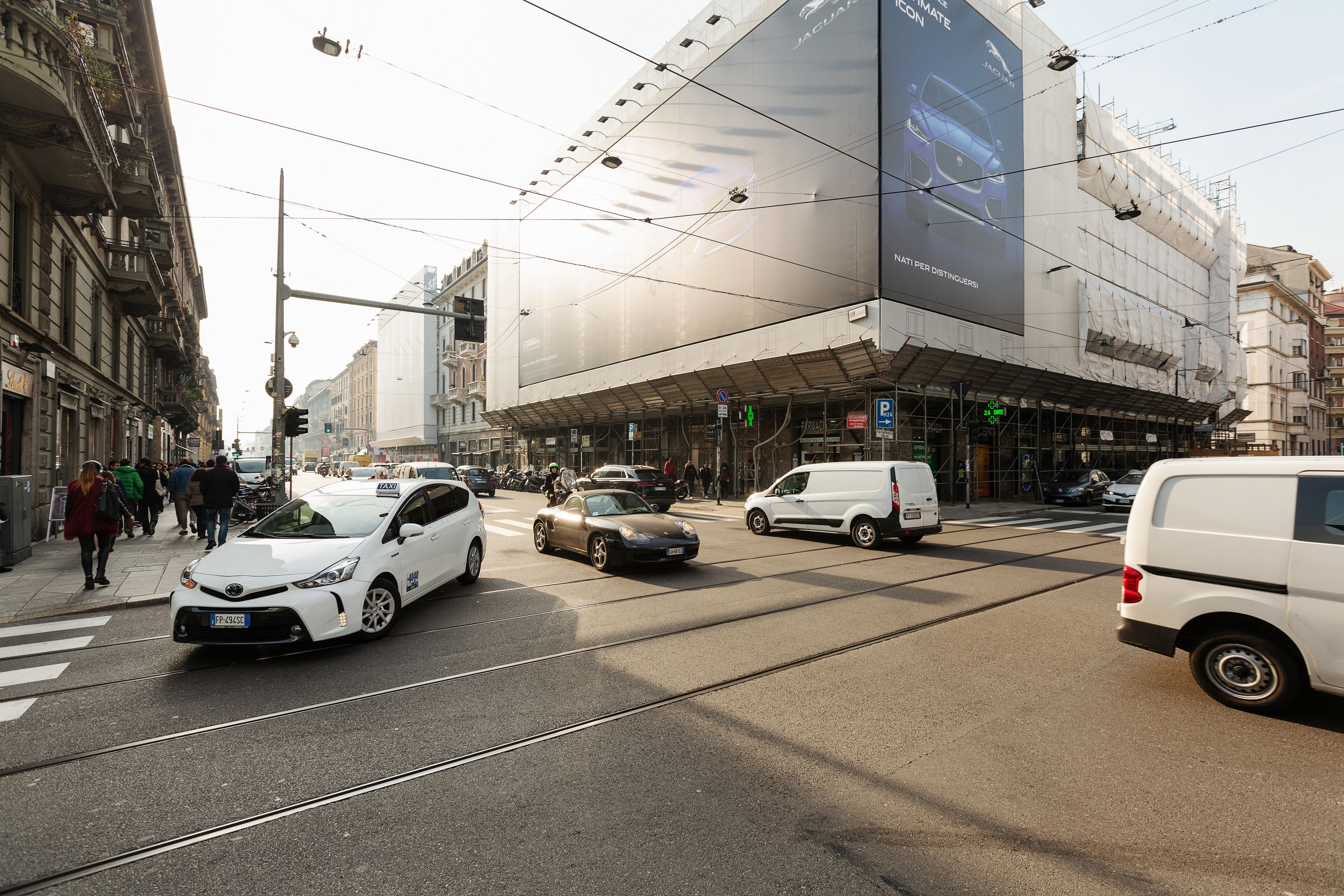 A busy urban street with tram tracks, cars, and pedestrians.