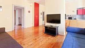 Una sala de estar con un televisor de pantalla plana, un sofá y una cama azul. Hay una zona de cocina con armarios rojos y un microondas.