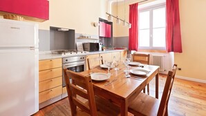 Una cocina moderna con armarios blancos, una mesa de comedor de madera dispuesta para cuatro personas y una cortina roja en la ventana.