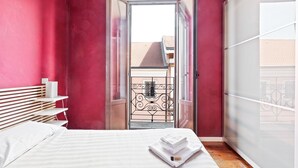 Un dormitorio con cama, mesita de noche, armario y vistas al exterior a través de una puerta.