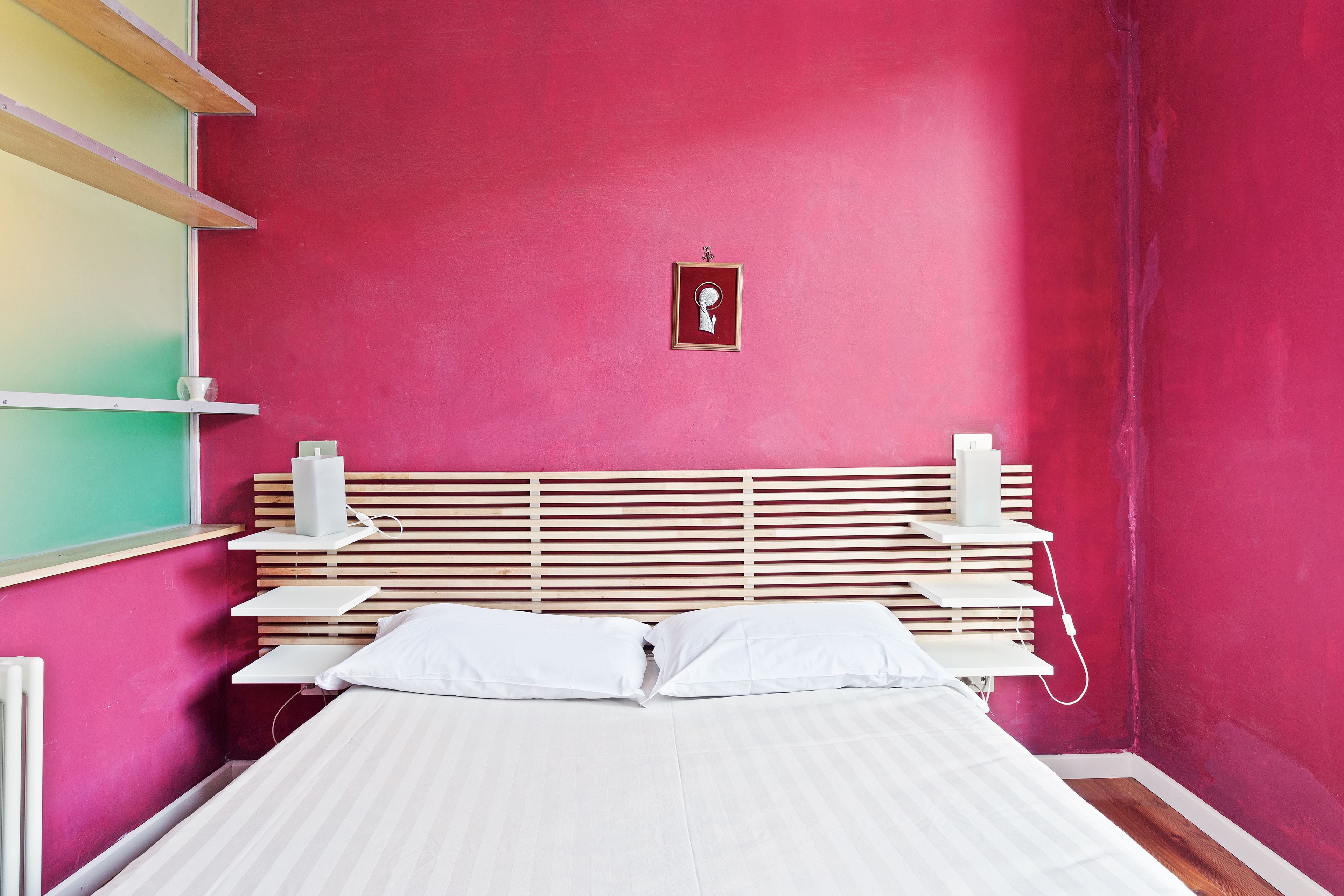 Un dormitorio con cabecera de madera con listones, ropa de cama blanca y un pequeño cuadro en la pared.