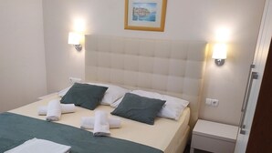 Een netjes opgemaakt bed met kussens en handdoeken, een nachtkastje en een wandlamp.
