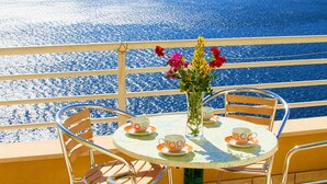 Een balkon met een tafel gedekt voor twee personen, een vaas met bloemen en uitzicht op zee.
