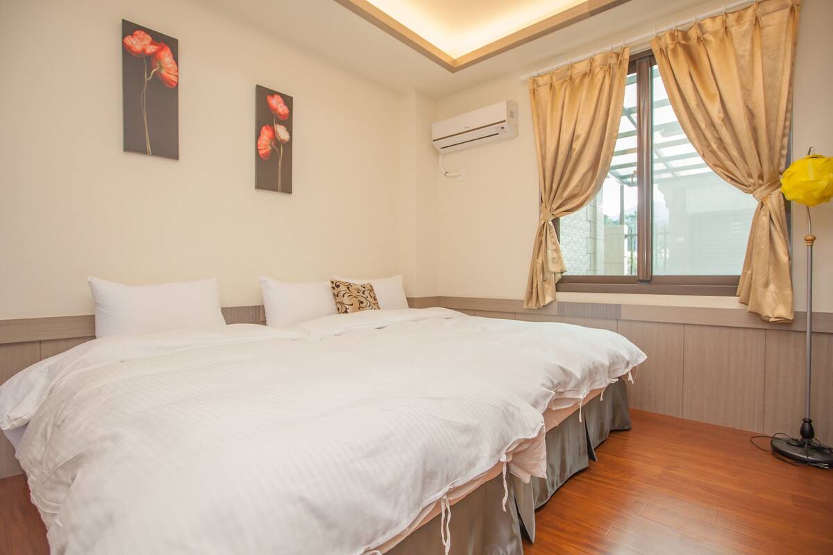 Un dormitorio con una cama grande, una ventana con cortinas, un equipo de aire acondicionado y obras de arte en la pared.