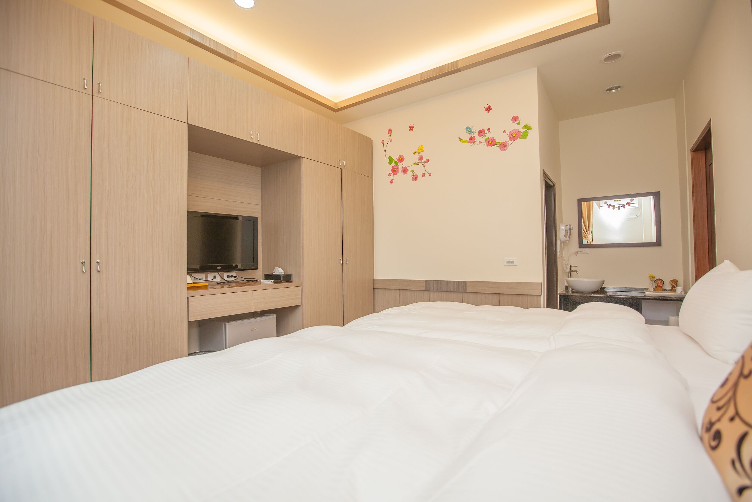 Hotelkamer met een bed, een bureau met een computer, een spiegel en een wand met bloemdecoraties.
