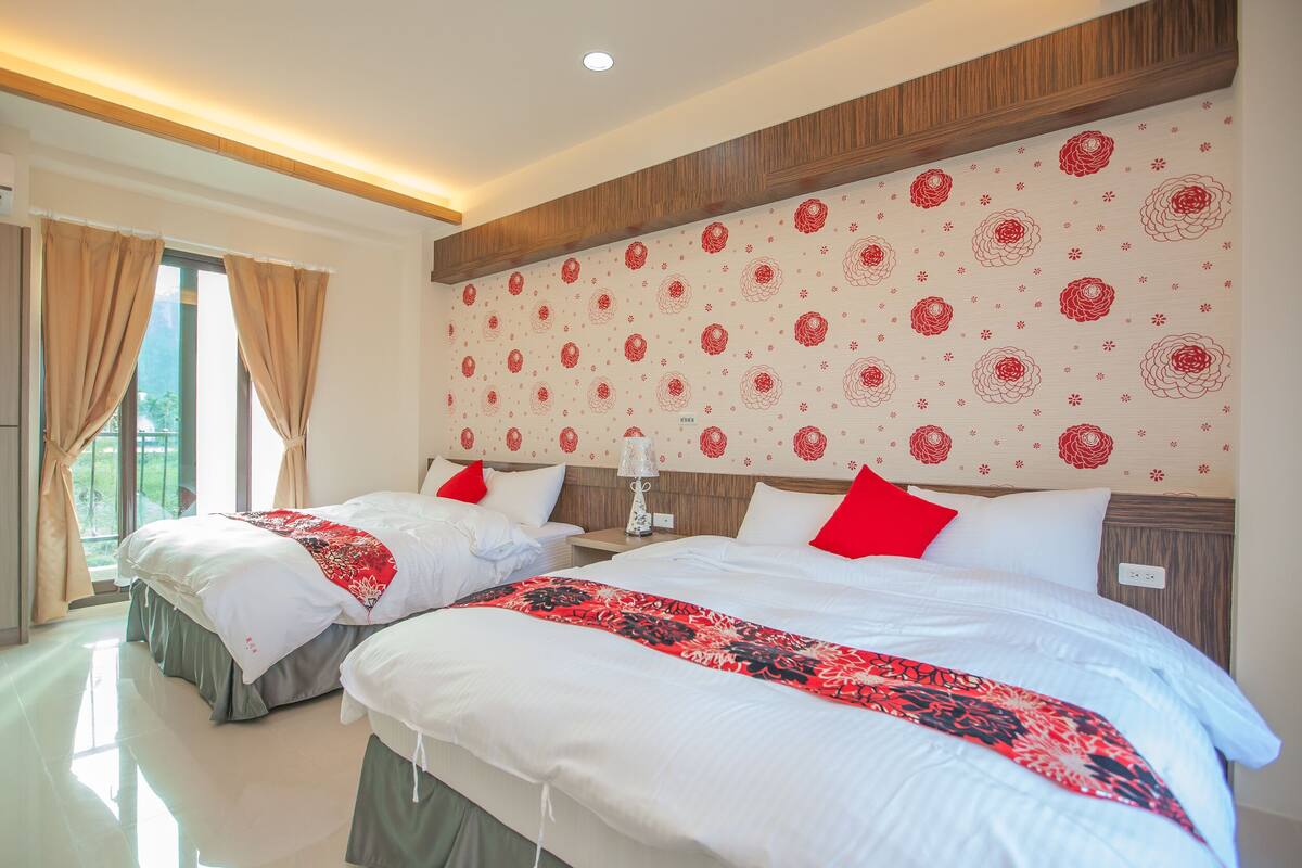 Habitación de hotel con dos camas, un ventanal con cortinas, un papel tapiz con diseño y cabecera de madera.