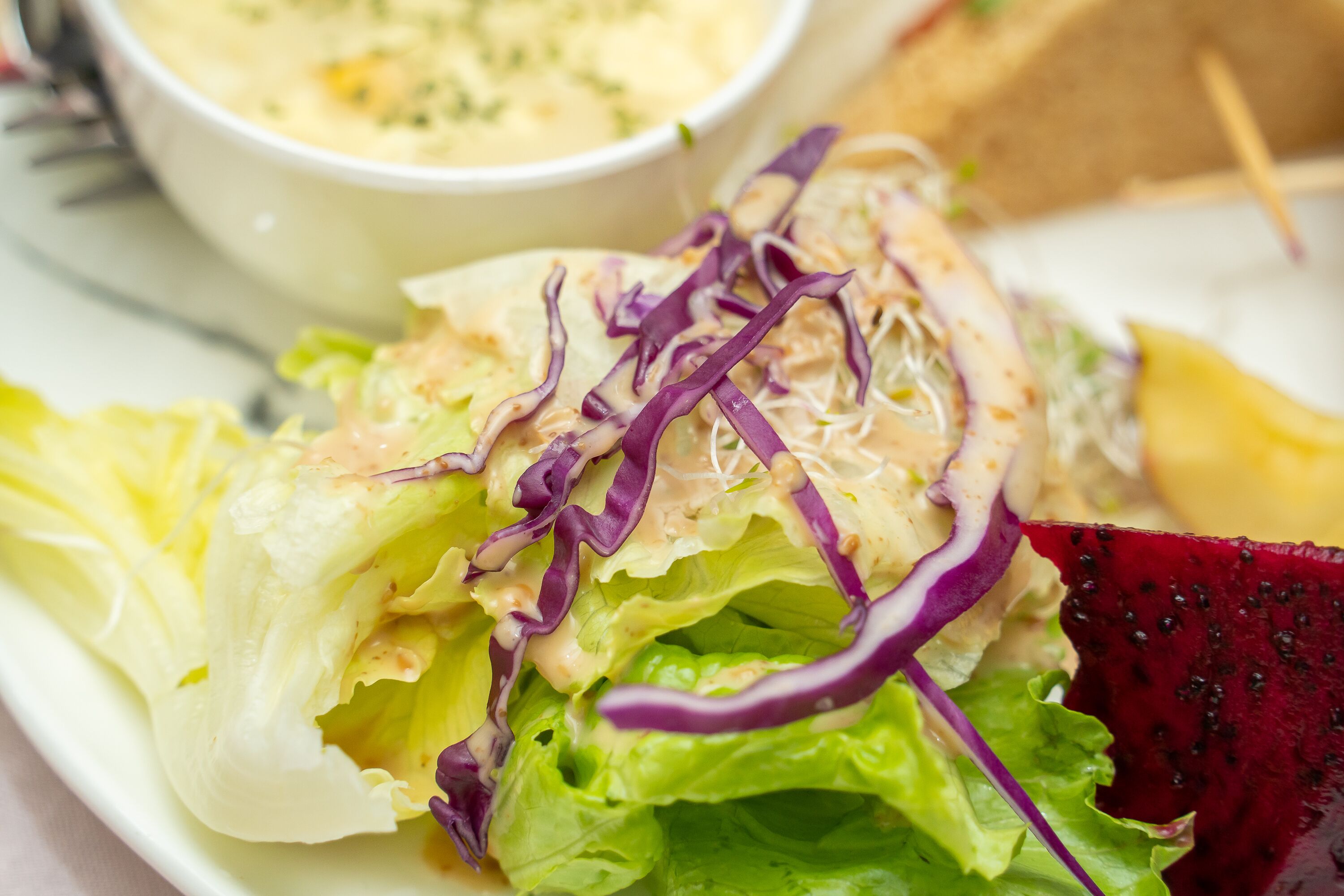 Een salade met gemengde bladgroenten en paarse kool, vergezeld van een dressing.
