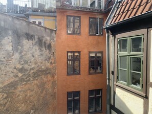 Une ruelle étroite entre deux bâtiments, où l’on peut observer un mélange d’architecture ancienne et moderne, avec de nombreuses fenêtres et un système de drainage apparent.