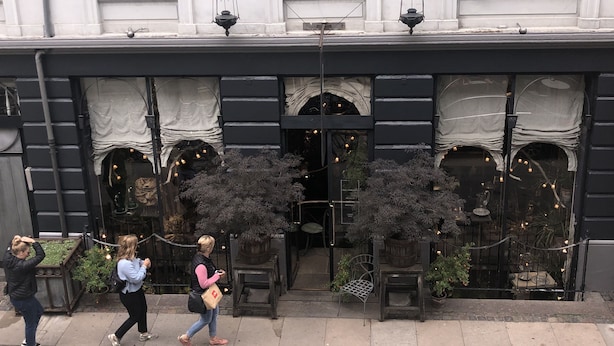 A building facade with large windows, a black awning, and outdoor seating area with potted plants. - Best Stay Copenhagen Ny Adelgade 7 2nd (Copenhagen)