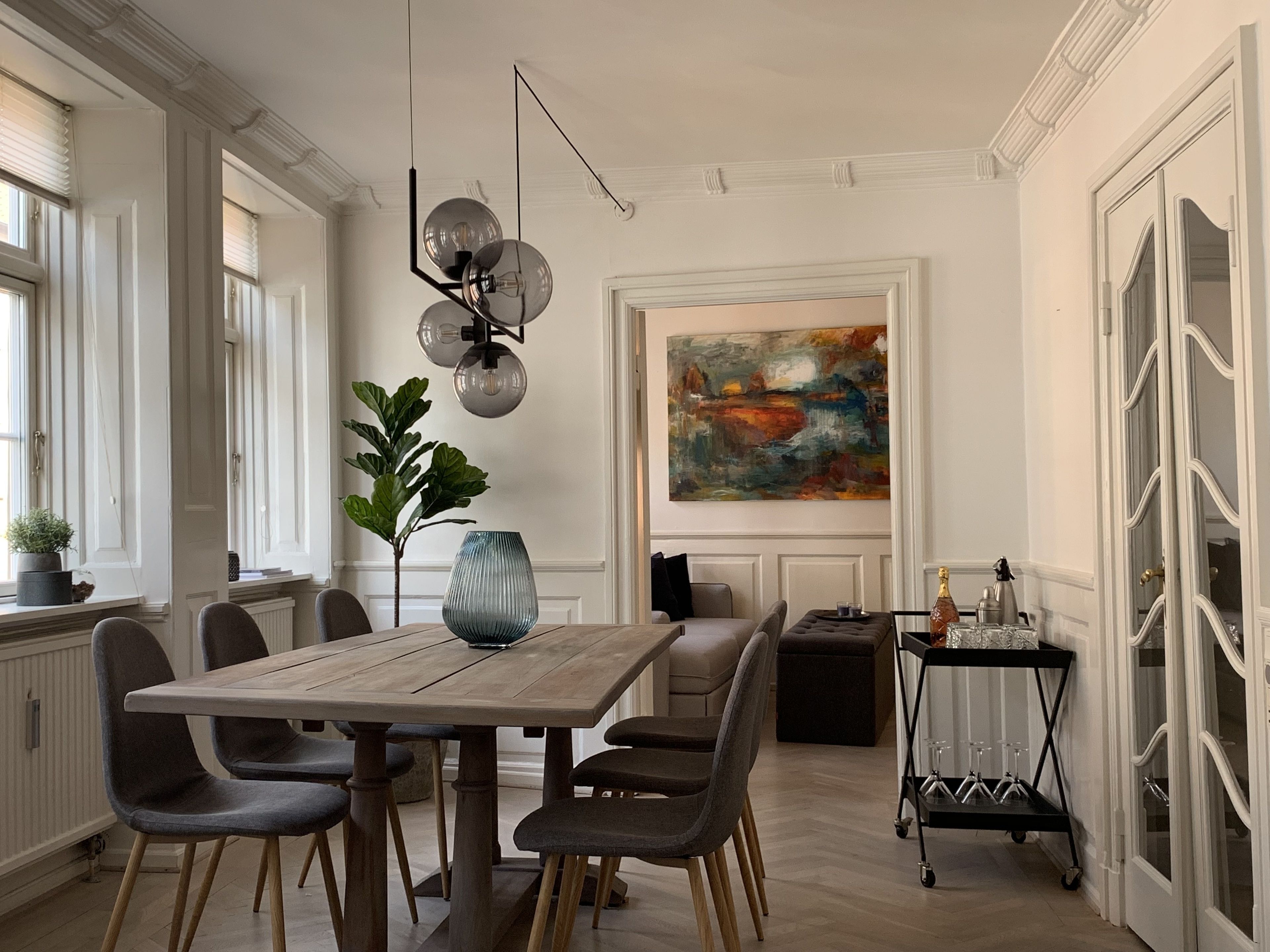 A dining area with a wooden table, grey upholstered chairs, a vase, and a modern pendant light.