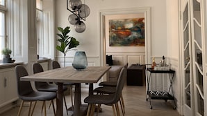 A dining area with a wooden table, grey upholstered chairs, a vase, and a modern pendant light. - Best Stay Copenhagen Ny Adelgade 7 2nd (Copenhagen)