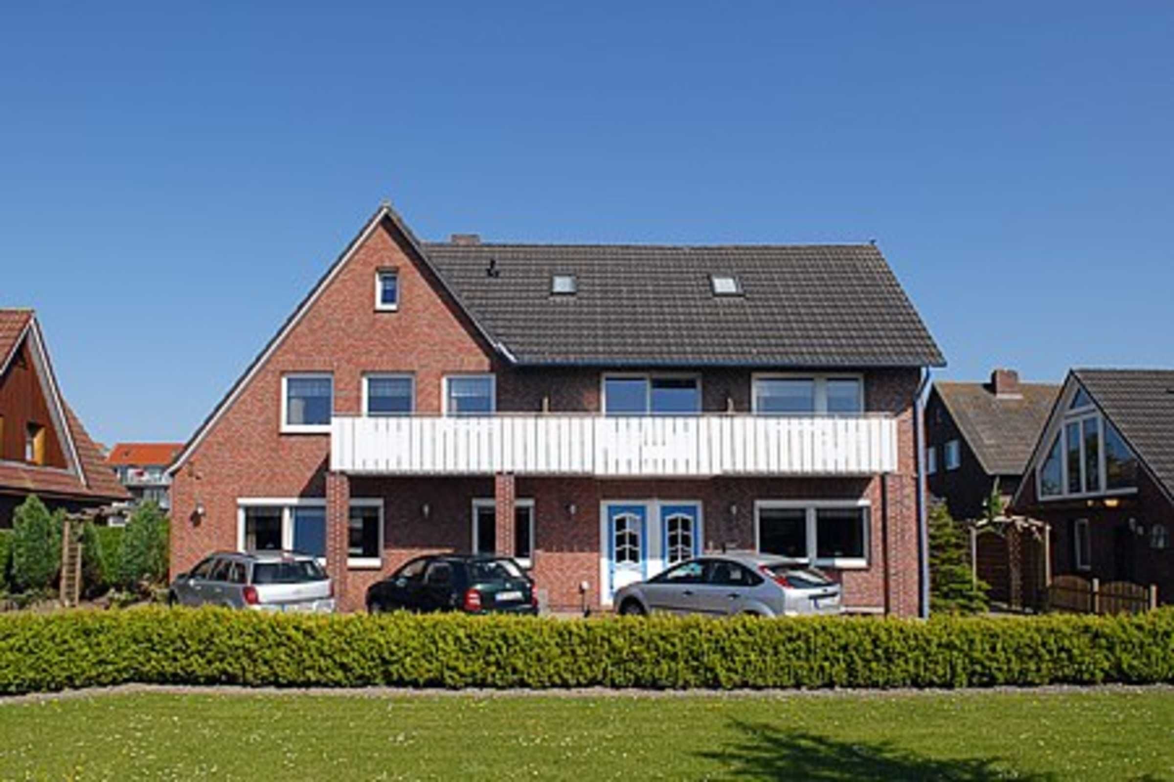 Une maison à deux étages avec une façade en briques, un toit plat et un porche avant couvert. Trois voitures sont garées devant.